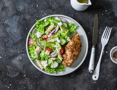 Mediterranean avocado pasta salad and baked chicken breast - healthy balanced lunch on a dark background, top viewの写真素材