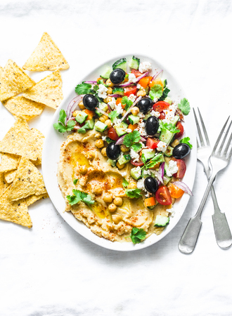 Loaded Greek salad hummus with corn tortilla chips on light background, top view. Delicious appetizer, tapas in a Mediterranean styleの写真素材