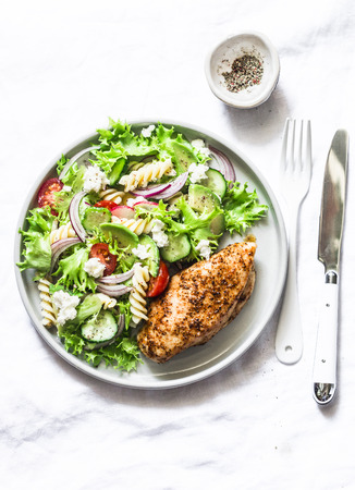 Mediterranean avocado pasta salad and baked chicken breast - healthy balanced lunch on a light background, top viewの写真素材