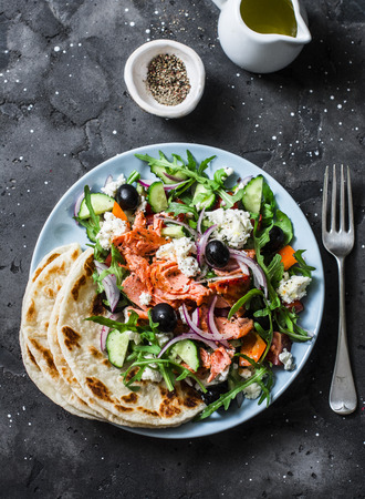 Greek salad with baked salmon on a dark background, top view. Healthy Mediterranean diet foodの写真素材