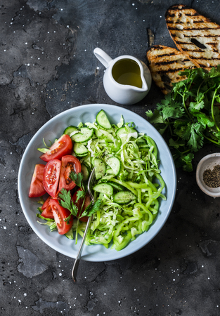 Fresh seasonal cabbage, cucumbers, peppers, tomatoes, cilantro salad and grilled bread on a dark background, top view. Healthy vegetarian diet foodの写真素材