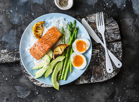 Healthy delicious balanced lunch - baked salmon, rice, asparagus, avocado and boiled egg on a dark background, top viewの写真素材