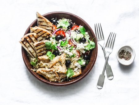 Mediterranean style lunch - couscous, cherry tomatoes, cucumbers, feta cheese, olives salad and lemon herbs roasted chicken breast on light background, top viewの写真素材