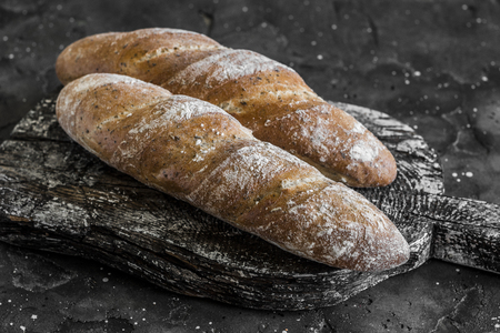 Homemade whole-grain baguettes with provencal herbs on rustic wooden board, on a dark backgroundの写真素材