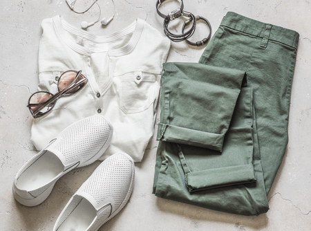 Women's summer clothes - olive cotton pants, white short sleeve t-shirt, white leather sports shoes, sunglasses, bracelets on a light background, top viewの写真素材