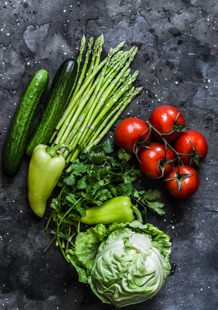 Fresh vegetables background - tomatoes, asparagus, cabbage, cucumbers, peppers and cilantro on a dark background, top view. Healthy food diet concept. Flat layの写真素材
