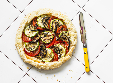 Grilled vegetables and mozzarella cheese puff pastry galette. Grilled eggplant, zucchini, tomatoes, cheese, thyme pie on a light background, top viewの写真素材