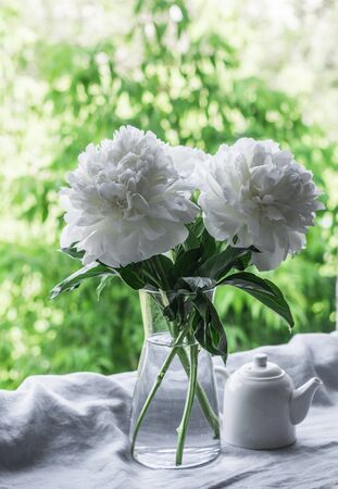 Bouquet of white peonies and a teapot on the window in the garden - a beautiful summer home still life. Flat lay, copy spaceの写真素材