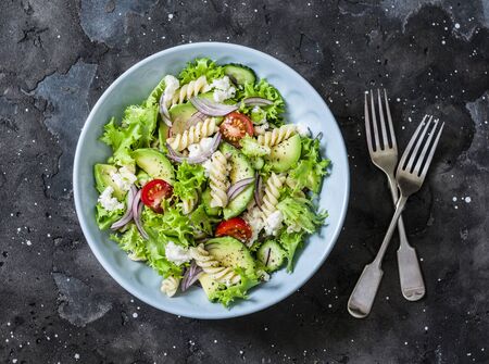Mediterranean pasta avocado salad on a dark background, top view. Vegetarian diet food conceptの写真素材