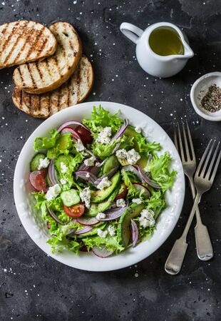 Vegetarian avocado, vegetables, feta cheese salad and grilled bread - delicious healthy lunch, snack on a dark background, top viewの写真素材
