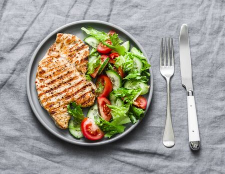 Grilled pork chops and tomatoes, cucumbers, greens salad on a gray background, top view. Healthy food diet conceptの写真素材