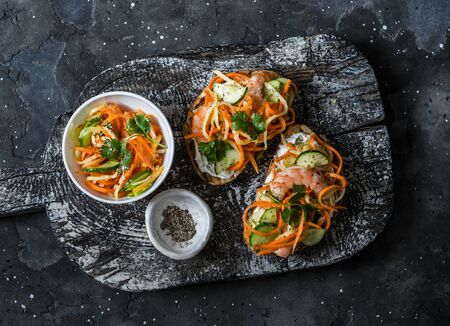 Shrimp banh mi sandwiches on rustic wooden cutting board on a dark background, top view. Grilled bread quickly pickled vegetables and prawns sandwichesの写真素材