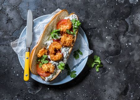 Po' boy sandwich with crispy cornmeal shrimp, tomatoes, cilantro and mayo herbs sauce on dark background, top viewの写真素材