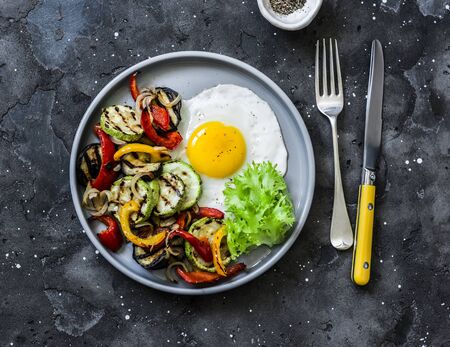 Delicious breakfast or snack - grilled vegetables and fried egg on a dark background, top viewの写真素材