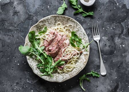 Peppered steak pasta. Spaghetti pasta with sliced beef steak and rocket salad on a dark background, top viewの写真素材