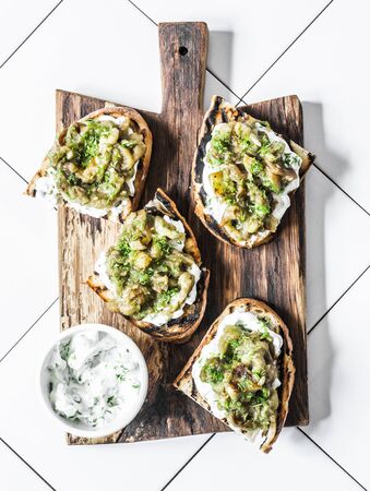 Smashed grilled eggplant bruschetta with yogurt herbs sauce - delicious appetizers, snacks, tapas on cutting board on a light background, top viewの写真素材