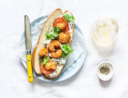 Po' boy sandwich with crispy cornmeal shrimp, tomatoes, cilantro and mayo herbs sauce on light background, top viewの写真素材