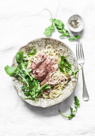 Peppered steak pasta. Spaghetti pasta with sliced beef steak and rocket salad on a light background, top viewの写真素材