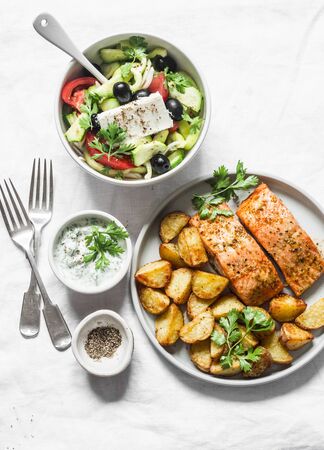Mediterranean lunch table - baked lemon salmon with potatoes, greek salad, tzadziki sauce on light background, top view. Flat layの写真素材