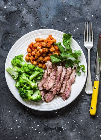 Grilled beef steak, spicy stewed chickpeas, broccoli - delicious healthy lunch on a dark background, top viewの写真素材