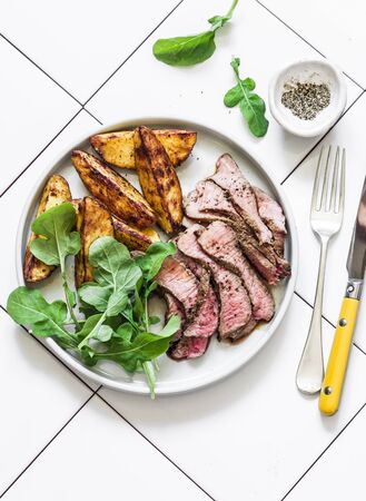 Beef steak and roast new potatoes - delicious lunch on a light background, top viewの写真素材