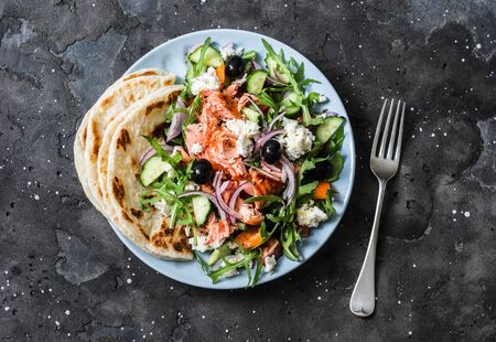 Healthy diet lunch - baked salmon, fresh vegetables, feta cheese salad on a dark background, top viewの写真素材