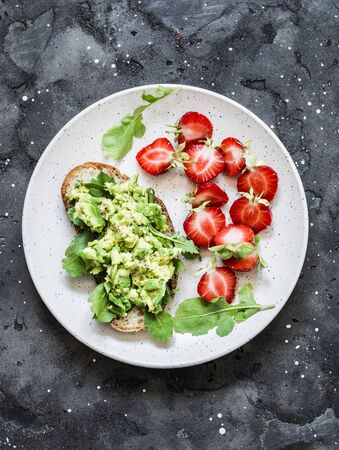 Healthy snack, breakfast - sandwich with avocado and fresh strawberries on a dark background, top viewの写真素材