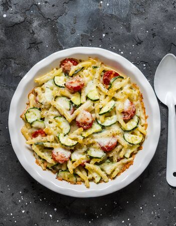 Roasted zucchini and cherry tomatoes baked mac and cheese  on the dark background, top view. Vegetarian healthy lunchの写真素材