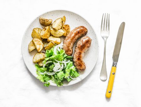 Roasted turkey sausages with baked potatoes and green salad - delicious lunch, snack, tapas on a light background, top viewの写真素材