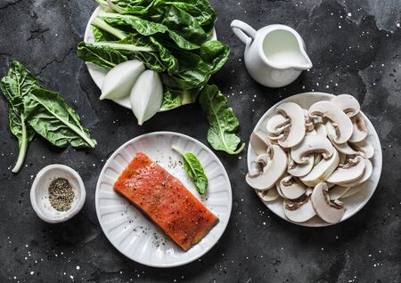 Raw ingredients for cooking salmon with creamy spinach mushrooms sauce on a dark background, top view. Salmon florentine lunch. Spinach, mushrooms and salmon fishの写真素材