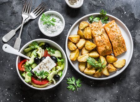 Mediterranean lunch table - baked lemon salmon with potatoes, greek salad, tzatziki sauce on dark background, top view. Flat layの写真素材