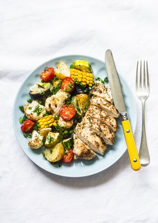 Chicken breast baked with potatoes, cauliflower, corn, eggplant, zucchini, cherry tomatoes on a light background, top view. Healthy food diet conceptの写真素材