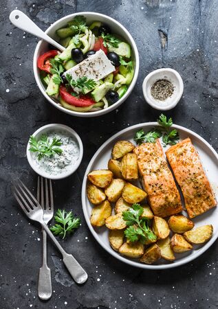 Mediterranean lunch table - baked lemon salmon with potatoes, greek salad, tzatziki sauce on dark background, top view. Flat layの写真素材