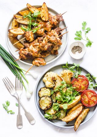 Meat skewers kebab with baked potatoes and roasted zucchini, tomatoes, cauliflower on a light background, top view. Delicious tapas, appetizers in mediterranean styleの写真素材