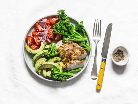 Baked chicken breast, broccoli, tomatoes, avocado salad on light background, top view. Balanced healthy eating buddha bowlの写真素材