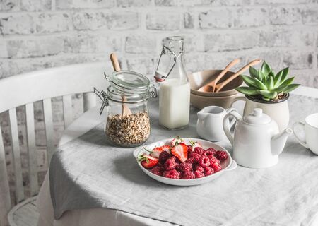 Breakfast served table - granola, milk, fresh raspberries and strawberries in the bright kitchen. Flat layの写真素材