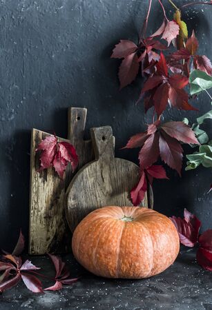Fall still life. Rustic cutting boards, leaf branches, pumpkin on the table, on a dark background. Copy space. Flat layの写真素材