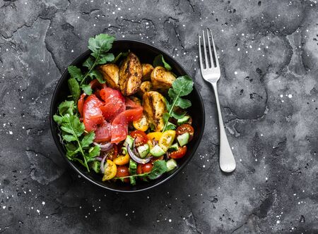 Smoked salmon, baked potatoes, fresh vegetables salad breakfast bowl on a dark background, top viewの写真素材
