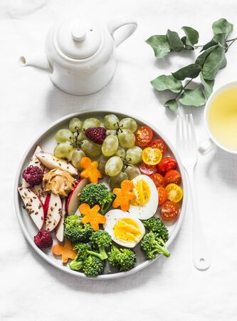 Delicious healthy women's, children's breakfast, snack - vegetables, fruits, berries, boiled egg and green tea on a light background, top viewの写真素材