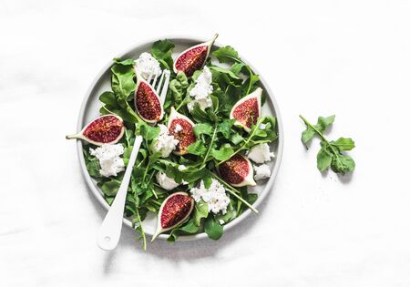 Figs, goat cheese, arugula salad on light background, top view. Delicious breakfast, snack, appetizer, tapasの写真素材