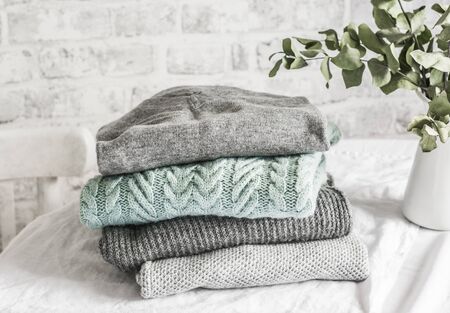 Stack of cozy winter autumn sweaters pullovers on the table on a light backgroundの写真素材