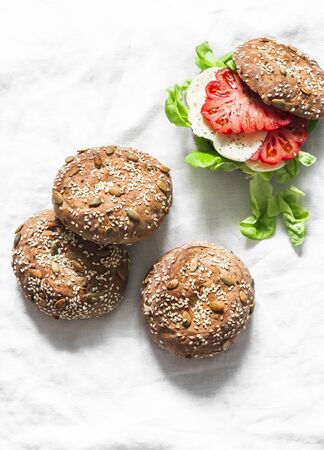 Multigrain multiseed fitness buns and green salad tomato homemade cheese sandwich on light background, top view. Healthy diet food conceptの写真素材