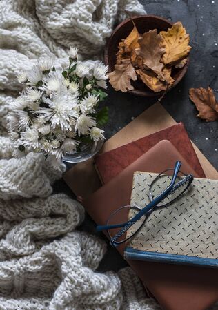 Stack of books, dry autumn leaves, knitted plaid - cozy home still life on a dark background, top view. Flat layの写真素材