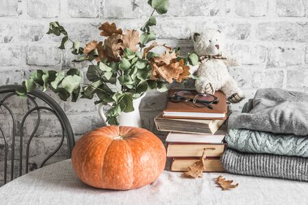 Autumn cozy home still life. Pumpkin, dry branch pitcher, stack of books, pile of winter autumn sweaters,  teddy bear on the kitchen table. Flat layの写真素材