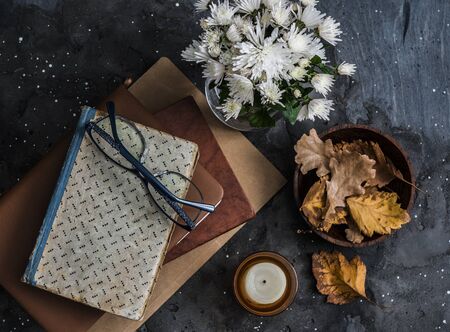 Stack of books, candle, autumn leaves - cozy home still life on a dark background, top viewの写真素材