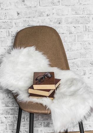 Brown soft loft style chair, fur rug, stack of books on light wall background. Interior concept, copy spaceの写真素材