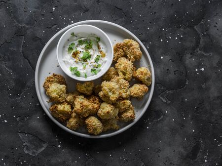 Baked crispy parmesan bread crumbs cauliflower bites with yogurt sauce on dark background, top viewの写真素材
