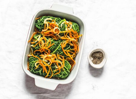 Raw uncooked vegetarian delicious lunch - roasted savoy cabbage stuffed spicy bulgur. Savoy cabbage bulgur rolls in baking pan on a light background, top viewの写真素材