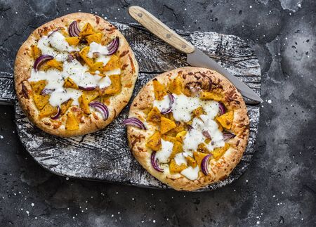 Cheesy autumn veggie flatbread. Pumpkin, sweet potato, red onion, mozzarella pizza on dark background, top viewの写真素材