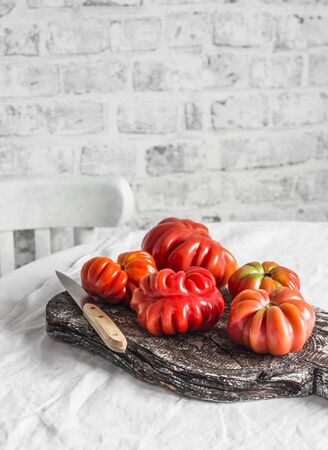 Heirloom ripe tomatoes on rustic cutting board to light the kitchen table on a light backgroundの写真素材
